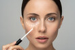 Close up of woman with natural makeup applying corrector on flawless fresh skin, doing make up. Girl after shower put concealer under eye area. Beauty face, skin care. Copy space, banner, advertising.