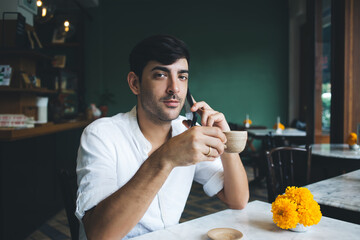 Charismatic confident businessman making phone call while drinking yummy hot beverage in cafe