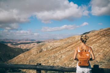 Wall Mural - Female backpacker enjoying free time for recreation in mountains environment of National Park, young travel woman looking around during hiking adventure trekking at nature with stunning altitude