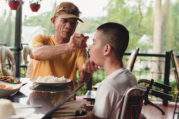 Wall Mural - Father feeding food to Disabled child on the wheelchair in home or restaurant,He practiced eating food,Special children's lifestyle,Lifestyle in the education age of kids,Happy disability kid concept.