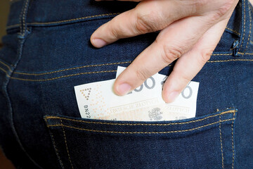 the man's right hand pulls two two hundred zloty bills from the back pocket of his blue jeans