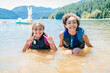 © Inti St. Clair - Smiling happy sisters in lifejackets swimming in lake water