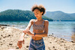 © Inti St. Clair - Teen girl with curly hair in a bikini and shorts putting on sunscreen on beach at lake in forest