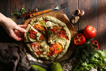 Wall Mural - Autumn vegetable pie with hand. Shortbread dough with tomatoes, zucchini, onion and pepper baked in the oven. Fresh herbs, garlic, fork on an old wooden table. Rustic. Copy space. Top view, flatlay