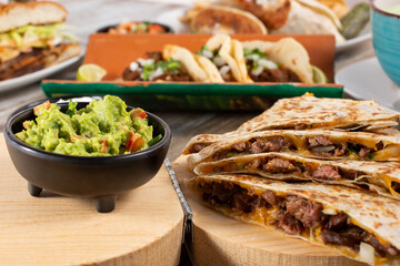 Wall Mural - A view of a table filled with a variety of popular Mexican entrees, featuring a quesadilla, in a restaurant or kitchen setting.