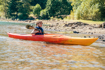 Girl paddling kayak on lake in forest in summer