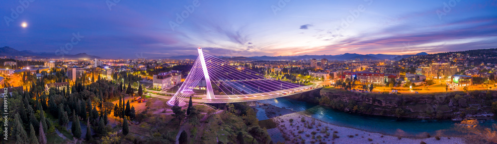 Obraz na płótnie Illuminated Millennium bridge over Moraca river in Podgorica Montenegro, at night. 180 degrees panorama of the city under sunset sky with moon in it. w salonie