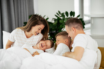 Wall Mural - Young family enjoying in bed. Happy parents with sons relaxing in bed..