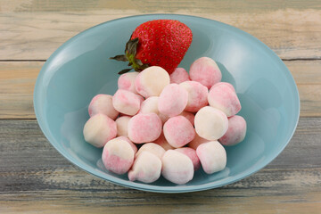 Wall Mural - Strawberry milkshake bonbon candy with fresh raw strawberry in blue bowl on table