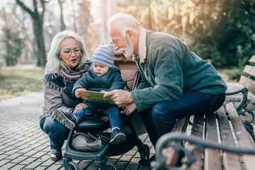 Wall Mural - Happy good looking senior couple husband and wife walking and playing with their adorable grandson in public city park