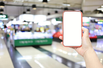 Hand of a man holding smartphone device in the Shopping mall background.