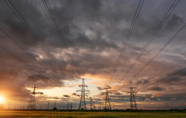 High-voltage power lines passing through a green field of wheat, on the background of a cloudy sky