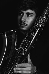 Wall Mural - Grayscale shot of a handsome guy holding his saxophone on a dark background