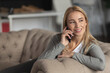 © kucherav - Gorgeous beautiful blonde woman with a wide smile communicates on the phone while sitting on the sofa at home