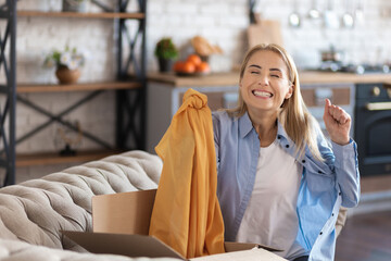 Wall Mural - Happy beautiful woman sitting on sofa and rejoicing in delivery with online sale