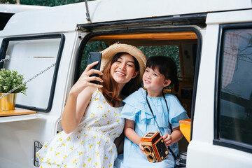 Asian mother and child taking selfie with smartphone in recreation vehicle.