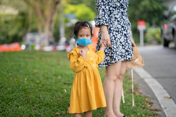 Wall Mural - little girl holding mother's hand wearing healthy  face mask stand along the road.