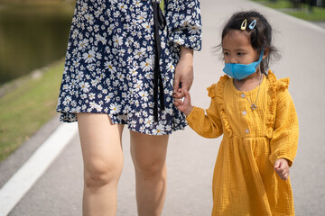 Wall Mural - little girl holding mother's hand wearing healthy  face mask walking on the road.