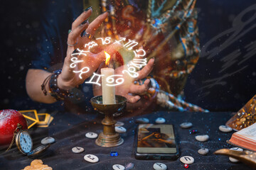 Astrology and online divination. A fortune teller does online fortune telling on photos from a smartphone. The zodiac circle is depicted above the candle. Close-up of hands and candles