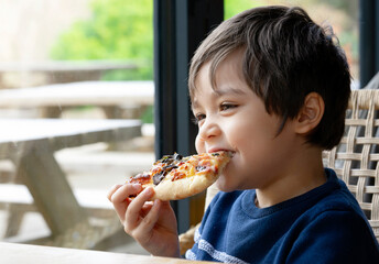 Cropped shot Cute kid boy eating home made pizza in the cafe,  Happy young boy biting off big slice of fresh made pizza in the restaurant, Family happy time concept