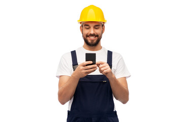 profession, construction and building - happy smiling male worker or builder in yellow helmet and overall with smartphone over white background