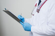 © Chanakon - Close up Asian bald Doctor in white coat, stethoscope, blue glove wearing.face mask writing something on clipboard isolated on white background.