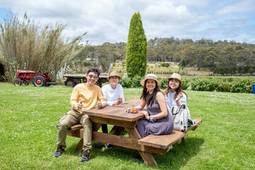 Poster - Trendy teenagers and parents rest on wooden bench at strawberry farm.