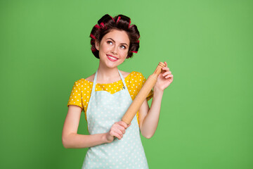 Sticker - Photo of charming cheerful lady curlers hairdo housewife hold rolling pin kitchen look up empty space dreamy thinking wear pinup dotted dress apron isolated green color background