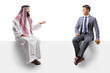 © Ljupco Smokovski - Saudi man in a thobe sitting on a blank panel and talking to a man in a suit