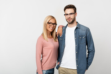 Smiling blonde woman in eyeglasses hugging man isolated on grey