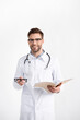 © LIGHTFIELD STUDIOS - Front view of smiling doctor with stethoscope holding eyeglasses and folder isolated on white