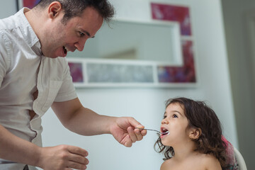 father feeds yogurt to a two-year-old girl sitting in a highchair