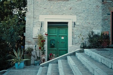 Wall Mural - A brick house with a green door and plants behind a staircase (Corinaldo, Marche, Italy)