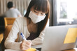 © dodotone - Young adult asian student female with face mask for virus corona or covid 19 study at cafe.