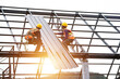 © somchai20162516 - Asian construction workers wear safety straps while working on the roof structure of the building at a construction site. Roofer, using a pneumatic nail gun, install roof tiles.