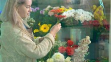 Skilled Woman Florist With Loose Fair Hair Takes Gerberas And Roses To Arrange Bouquet Behind Flower Shop Window Slow Motion