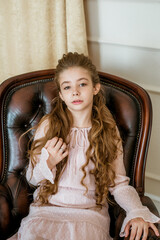 Lovely and elegant girl with long fair hair, in beautiful fashionable dresswith hairstyles in a classic light interior . Beauty and fashion. Children fashion