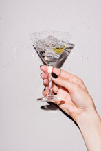Cropped View Of Woman Shaking Glass Of Martini With Olive Near Drops Of Alcohol On White