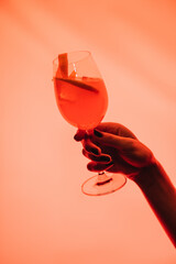 Woman holding glass with mixed cocktail and orange on pink