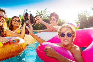 Wall Mural - Close photo of teenage children in water party with soda drink, lift hands and swim in inflatable doughnuts