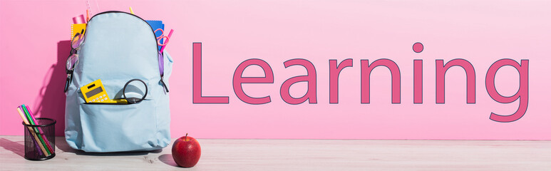 Canvas Print - horizontal image of blue backpack with school supplies near whole apple, pen holder with felt pens and learning lettering on pink