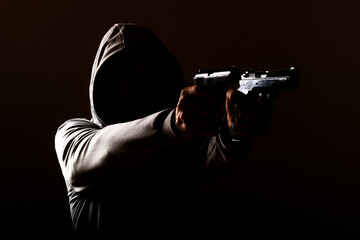 Wall Mural - dangerous hooded man threatens with a pistol shot in his hands, one