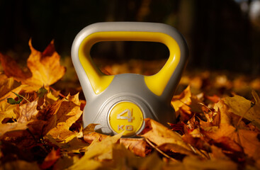 Heavy kettlebell with autumn leaves in a park. Healthy fitness lifestyle during fall season.