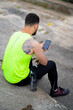 © Georgii - Male using sport training app in phone. Athletic guy sitting on stairs with bottle of water, back view