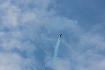 fighter plane flies up steeply at a air show with blue sky and clouds