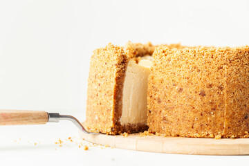 Wall Mural - Homemade classic New York cheesecake cut on the wooden board. Vanilla pie with cheese and crunchy crust on the whiite background. Close up, macro shot