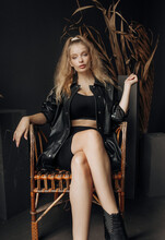 Luxury Blonde In A Black Suit Posing On A Straw Chair On A Black Background.