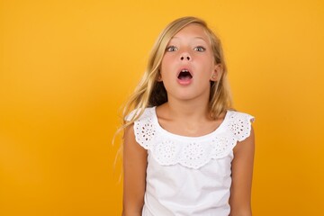 Emotional attractive Beautiful Caucasian young girl standing against yellow with opened mouth expresses great surprise and fright, stares at camera. Unexpected shocking news and human reaction.