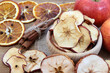 Dried apples in a wooden bowl surrounded by cinnamon sticks, fresh apples and dried oranges