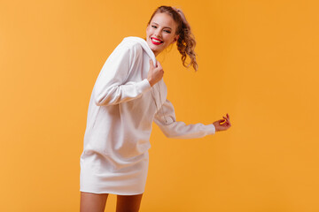 Wall Mural - Portrait of giggling female student in excellent mood. Curly blonde with ponytail dancing on isolated bright background